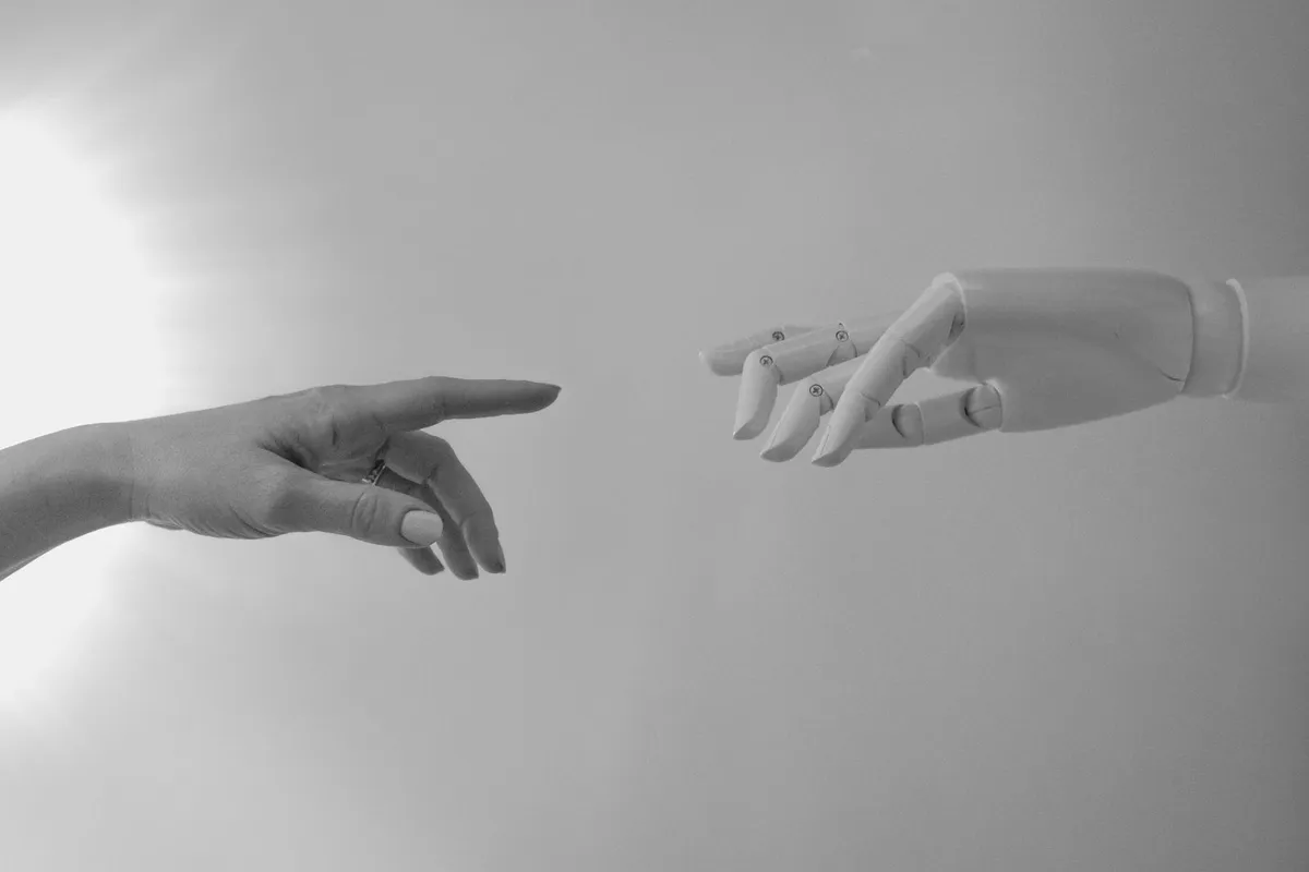 Mão humana e mão robótica em foto preto e branco simbolizando IA e humano